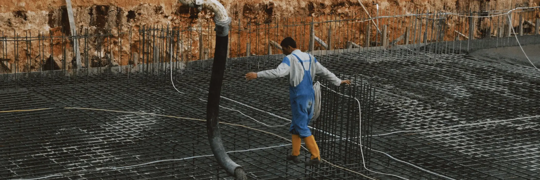 A worker in blue coveralls guides a concrete pump hose across a rebar mat as the pour begins.