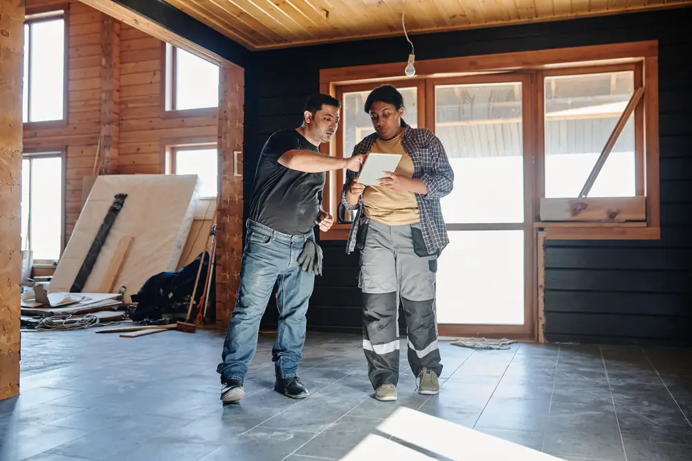 Two tradespeople inside a house under renovation; one points to something on a tablet the other is holding.